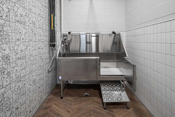 A stainless steel sink in a tiled room with a wooden floor.