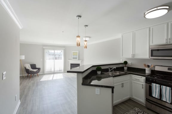 an empty kitchen and living room with white cabinets and black counter tops at Warner Center Townhomes, California