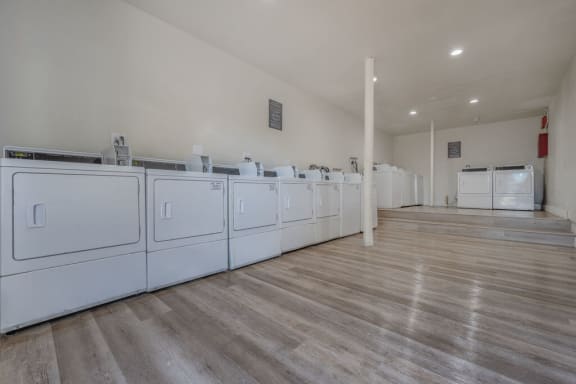 a row of white washers and dryers in a room with wood floors at The Hills Apartments at Thousand Oaks, Thousand Oaks, CA
