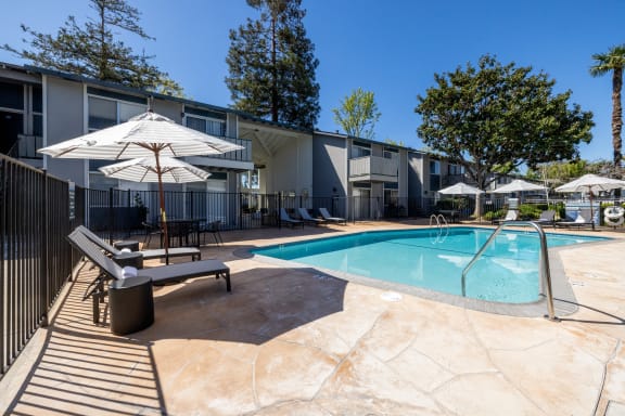 a swimming pool with chairs and umbrellas next to a building at Campbell West Apartments, Campbell, 95008