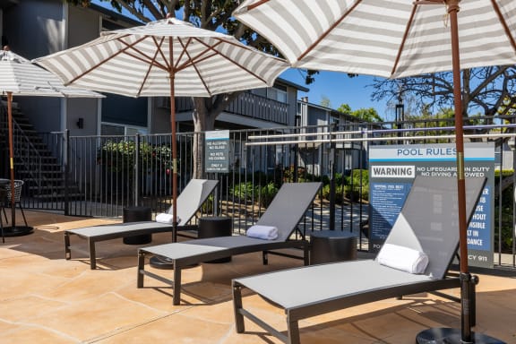 a group of lounge chairs with umbrellas in front of a building at Campbell West Apartments, Campbell
