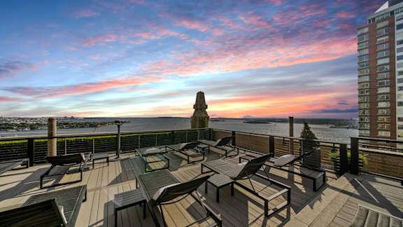 A rooftop patio with a table and chairs overlooking the water at One West, New York, NY,10004.