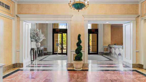A hallway with a chandelier, a potted plant, and a bench. at One West,  New York,10004