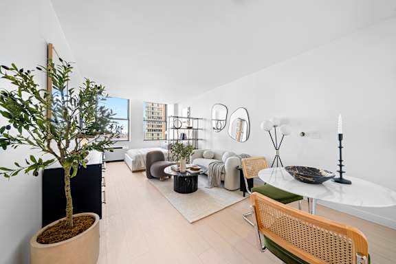 A living room with a tree in a pot, a white table, and a chair. at One West,New York, NY