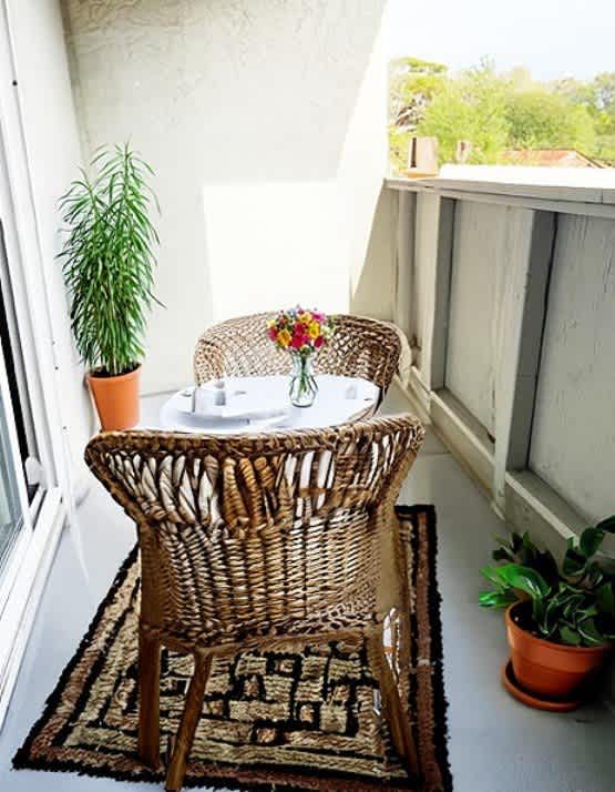 A balcony with a wicker chair and table with flowers on it.