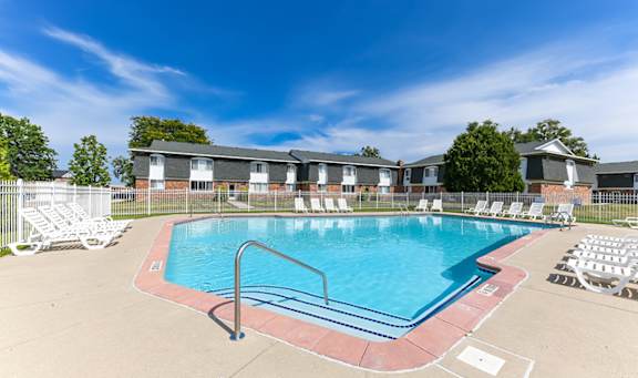 A swimming pool surrounded by chairs and a fence with houses in the background.