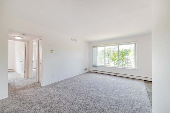 A large, empty room with a carpeted floor and a window.