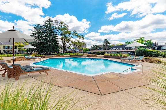 A large outdoor swimming pool surrounded by a concrete patio and deck chairs.