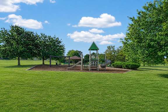 A playground with a green sign and slide in the middle of a grassy area.