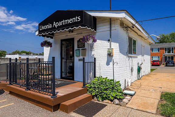A white building with a black fence and a sign that says Livonia Apartments.