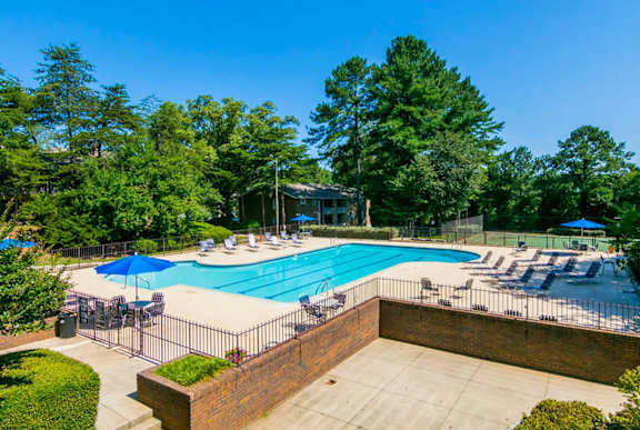A large swimming pool surrounded by trees and a brick wall.