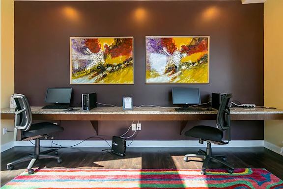 A room with a desk and two chairs with computers on it.