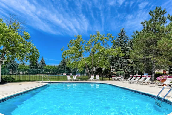 a swimming pool with chairs around it and trees in the background