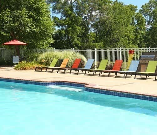 A pool with a red umbrella and colorful chairs.