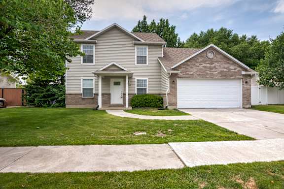 A two-story house with a garage is surrounded by a green lawn.