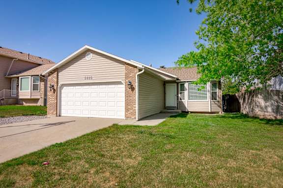 A house with a white garage door is surrounded by a green lawn.