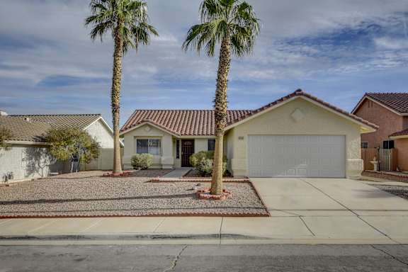 A house with a red tile roof and a white garage door is surrounded by palm trees.