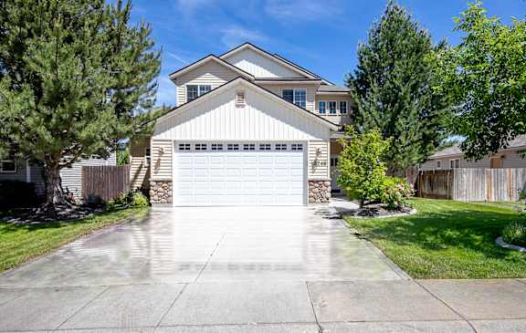 A two-story house with a garage is surrounded by a fence and trees.