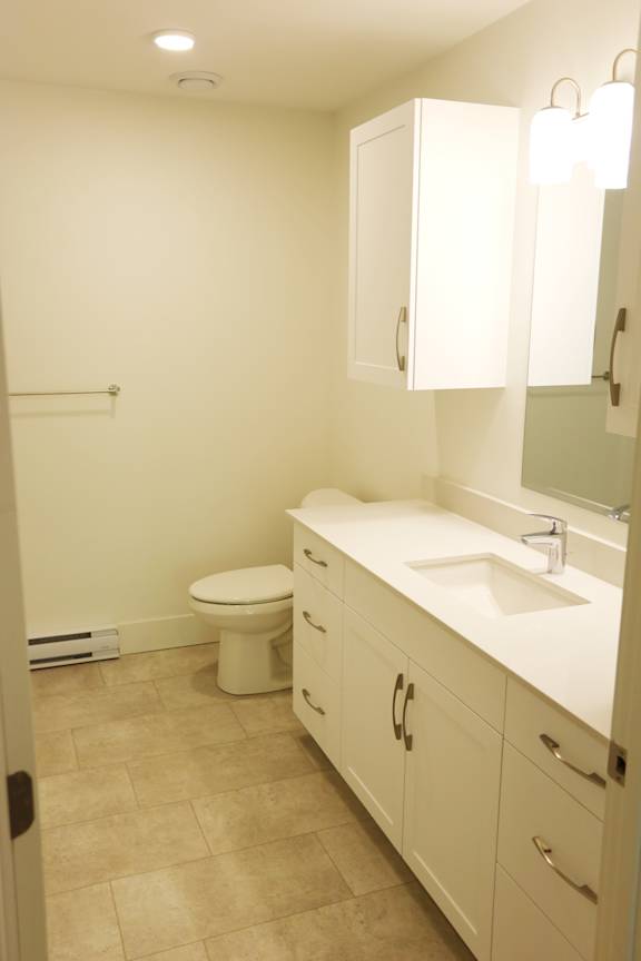 A white bathroom with a toilet, sink and cabinets.