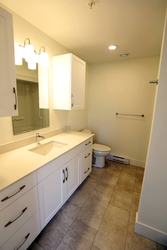A bathroom with a sink, mirror, toilet and a towel bar.