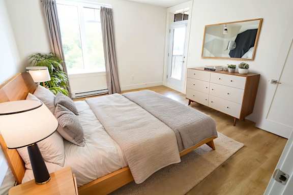 A bedroom with a bed, nightstand, and a plant.