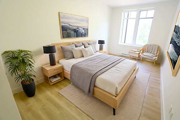 A bedroom with a large bed, a potted plant, and a painting on the wall.