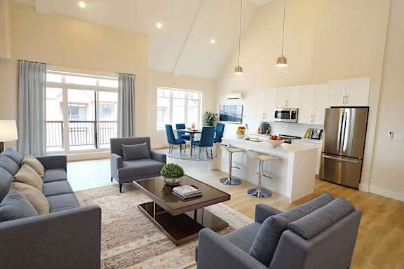 A modern living room with a grey sofa, a coffee table, and a kitchen in the background.