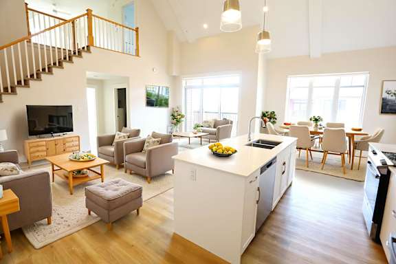 A well-lit, spacious open-plan living and kitchen area with wooden floors and furnished with a variety of seating options.