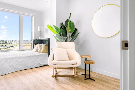 A white chair with a green plant in a vase sits in a room with a large window.