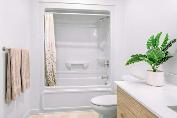 A white bathroom with a towel hanging on the wall and a plant on the counter.