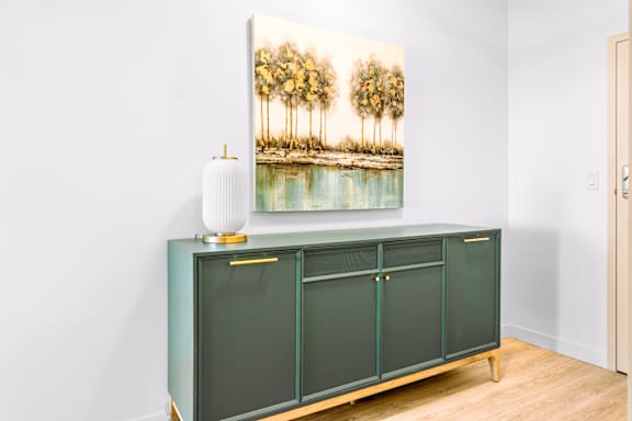 A green cabinet with a painting of palm trees on the wall above it.