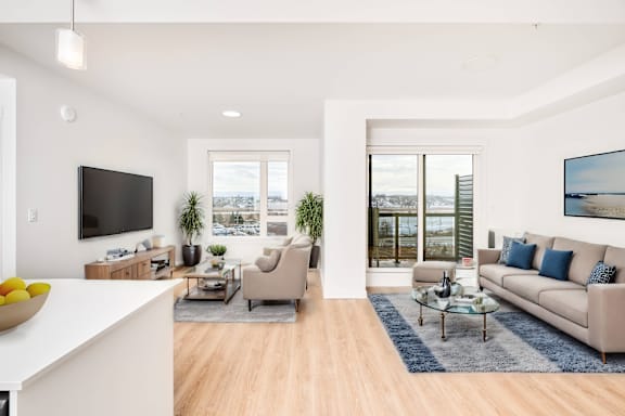 A modern living room with a flat screen TV, a sofa, a coffee table, and a large window.
