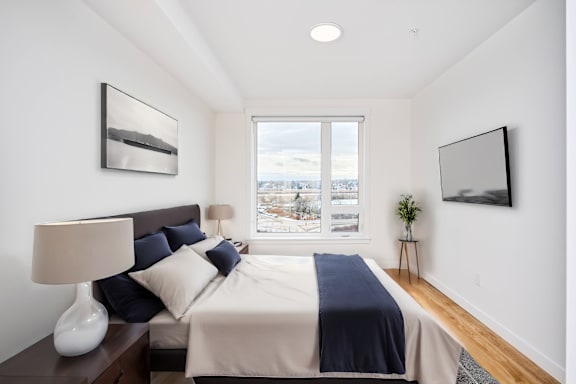 A bedroom with a large bed and a window overlooking a cityscape.