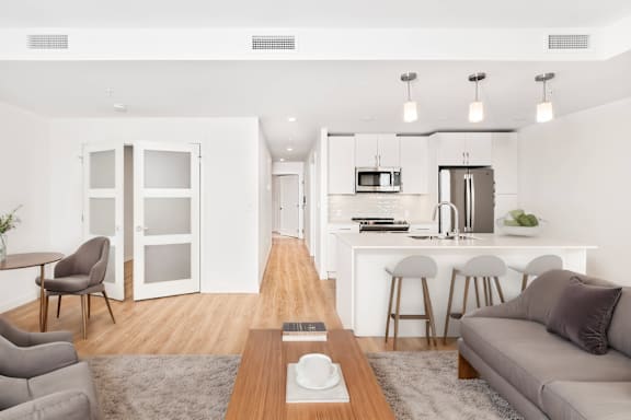 A modern living room with a grey couch, a coffee table, and a kitchen area in the background.