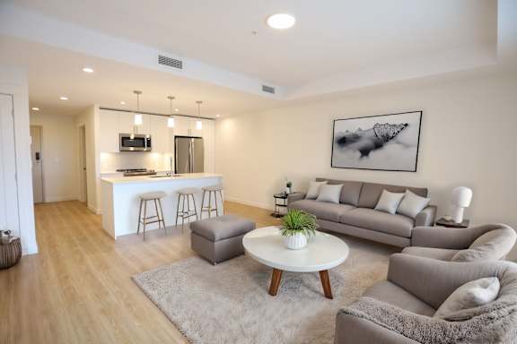 A modern living room with a grey couch, a white coffee table, and a bar area in the background.