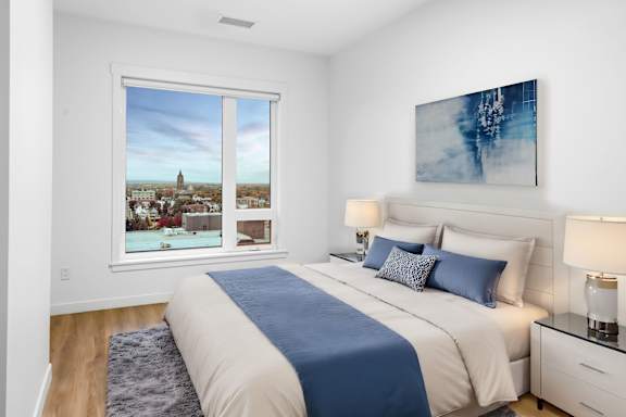 A bedroom with a large bed and a view of a city through the window.