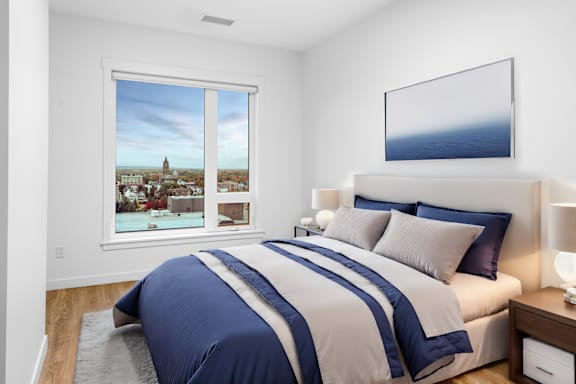 A bedroom with a large bed and a view of a town through the window.