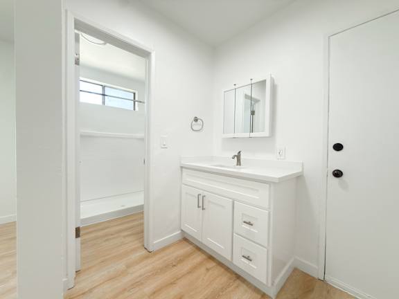 A white bathroom with a sink, mirror, and wooden floors.