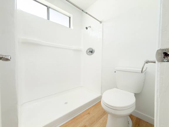 A white toilet in a small bathroom with a white tub and a window.