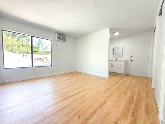 A room with wooden flooring and a window overlooking a backyard.