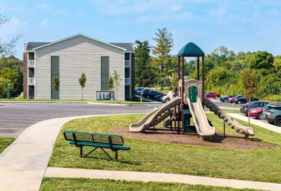 A playground with a green slide and a green bench in front of a building.