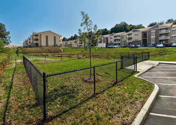 A black fence surrounds a green field with apartment buildings in the background.
