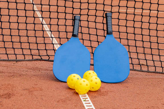 Two blue paddles and three yellow balls on a red surface.