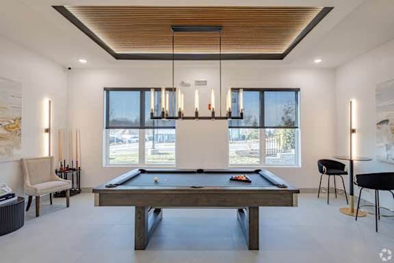 A billiard table is in the middle of a room with a pool table light and a chair.
