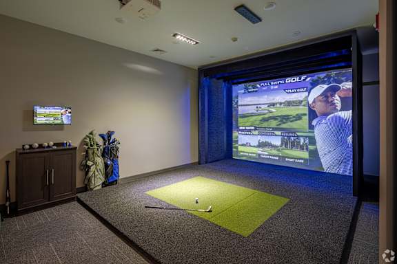 A golf simulator room with a screen showing a golfer on the course.