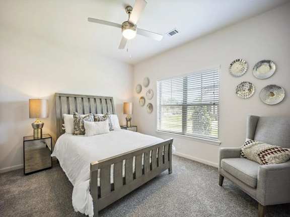 A bedroom with a bed, chair, and ceiling fan.
