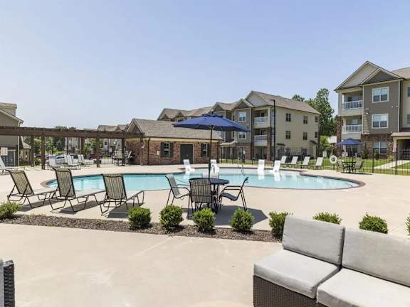 A pool surrounded by chairs and a bench in front of apartment buildings.
