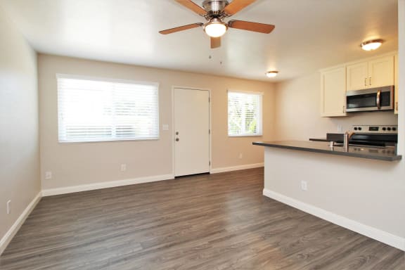 an empty living room with a kitchen and a ceiling fan