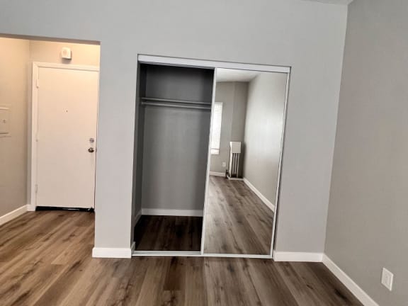 a mirrored closet in a room with wood flooring and a door to a hallway