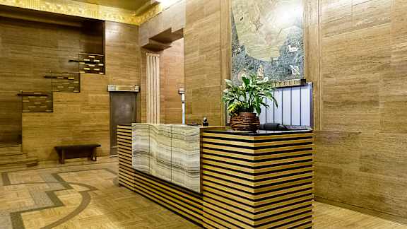 A reception desk with a plant on top and a painting on the wall.